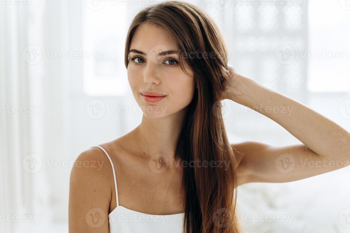 thuisportret van een schattige bruinharige vrouw met een gezonde huid die met kalme uitdrukking voor de camera zit terwijl ze de ochtend doorbrengt in haar appartementen. schoonheid en vrouw uiterlijk concept foto