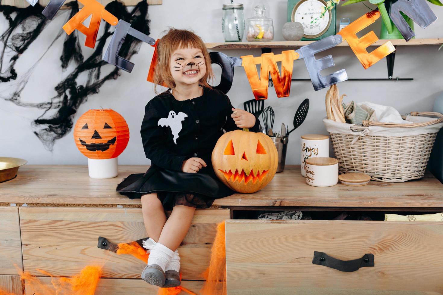 klein grappig meisje dat naast de pompoen zit en gelukkig lacht. - Halloween-concept foto