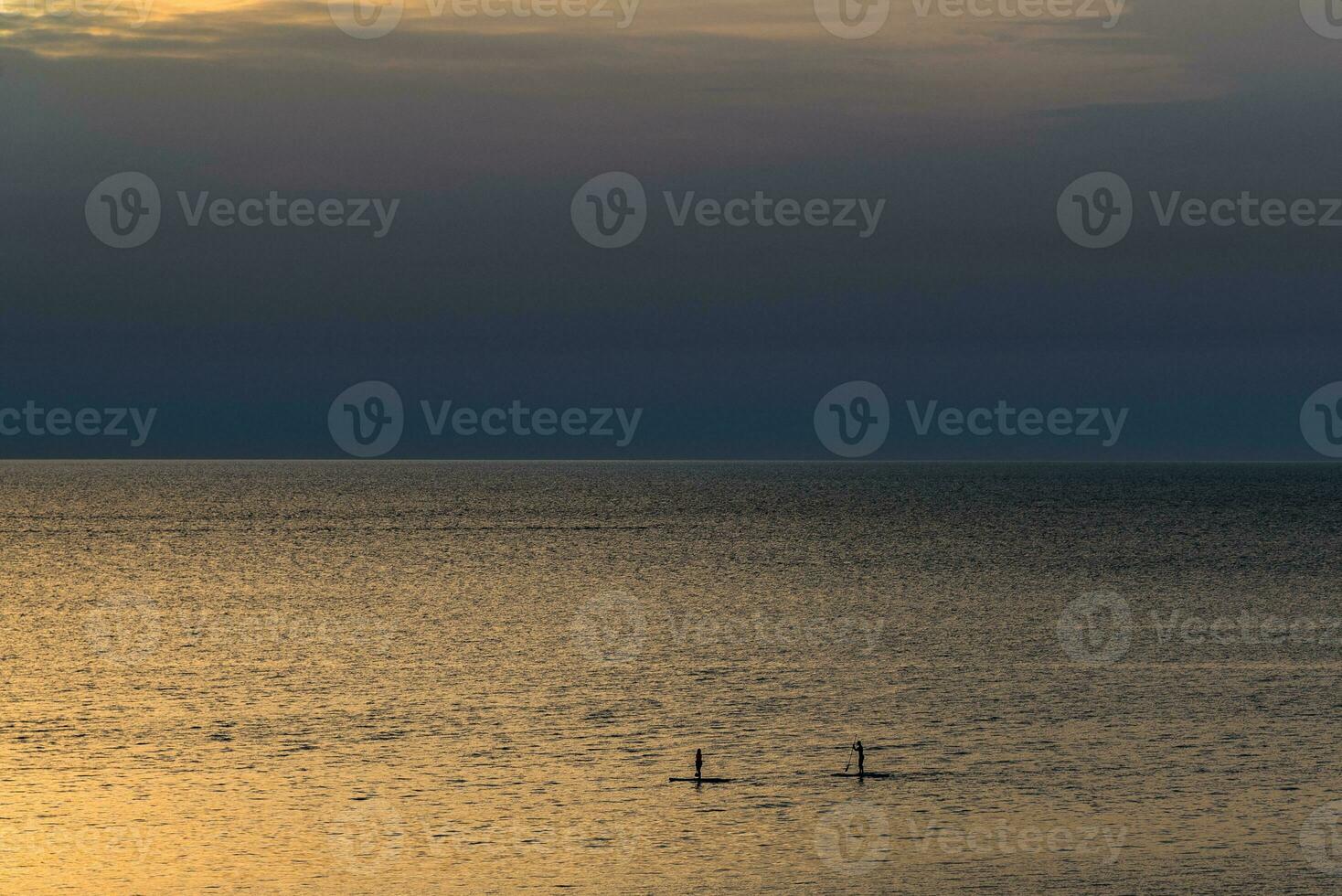 surfers Aan de kalmte zee gedurende de zonsondergang foto