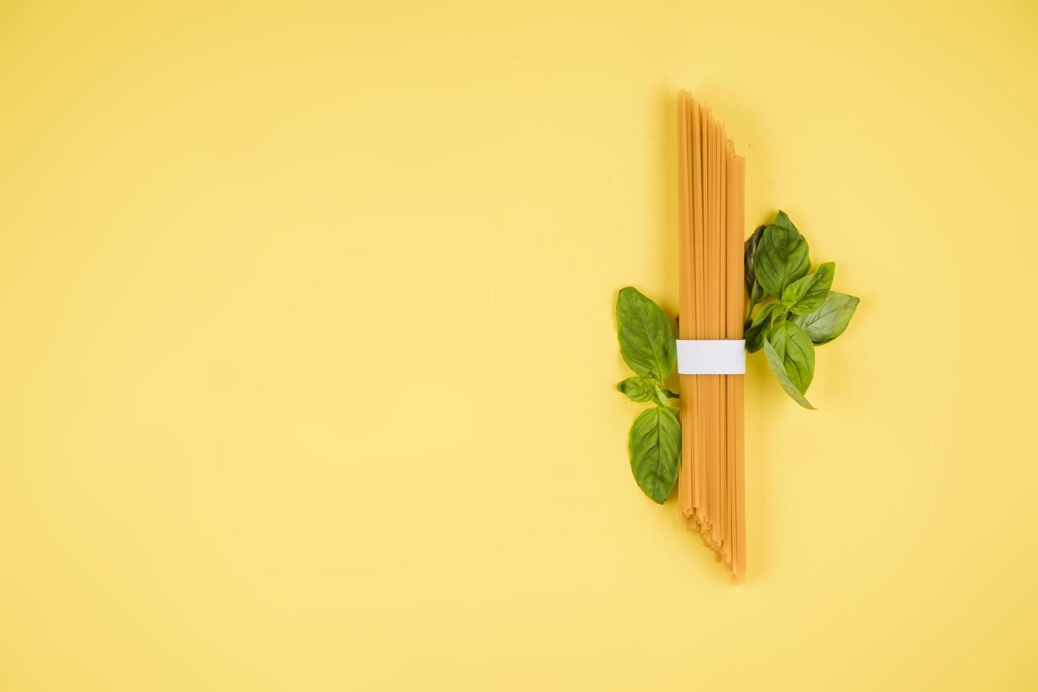 spaghetti, basilicum op een gele achtergrond. bovenaanzicht. kopieer ruimte voor tekst. foto