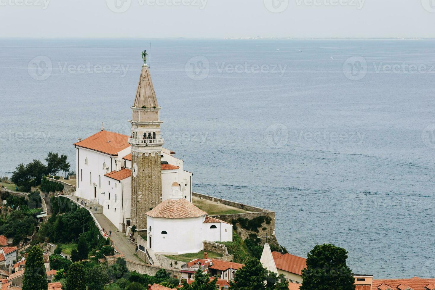 heilige George kathedraal in piran met kalmte zee Aan de achtergrond en groen bomen dichtbij foto