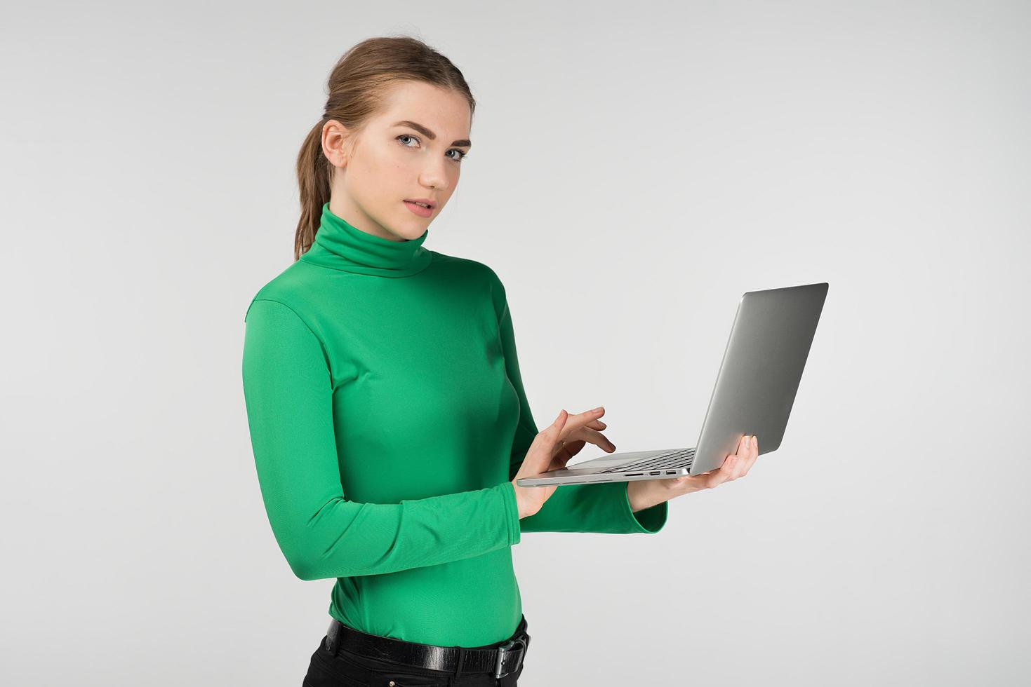 vrouw in halve draai werkt op een laptop die hem in haar handen houdt terwijl ze tegen de witte achtergrond staat. kijkt naar de camera foto