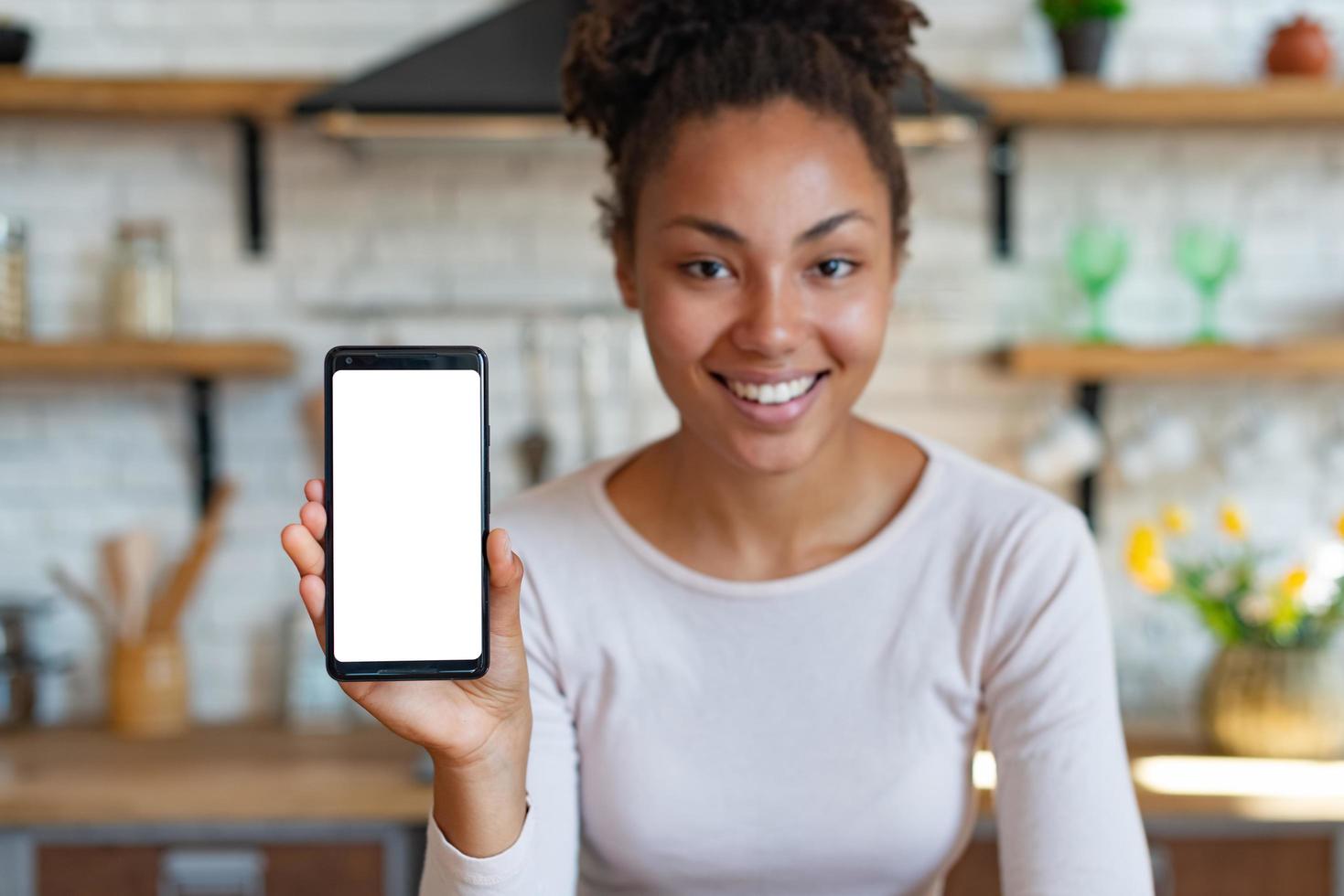 jonge lachende vrouw zit en toont een mockup met wit scherm van mobiele telefoon. - afbeelding foto
