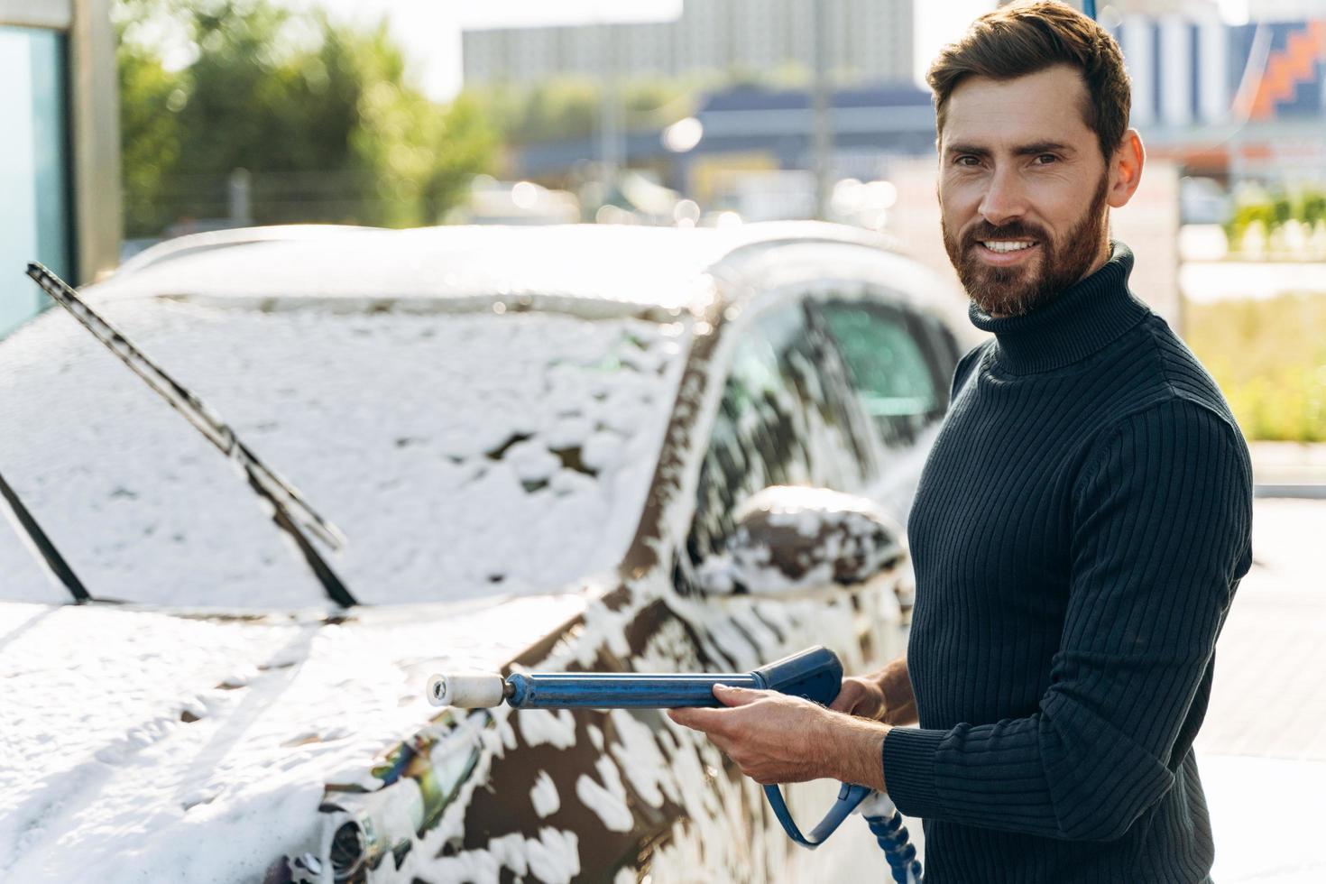 taille portret van de man die naar de camera glimlacht terwijl hij een hogedrukspuit vasthoudt voor het wassen van de auto. concept desinfectie en antiseptische reiniging van het voertuig foto