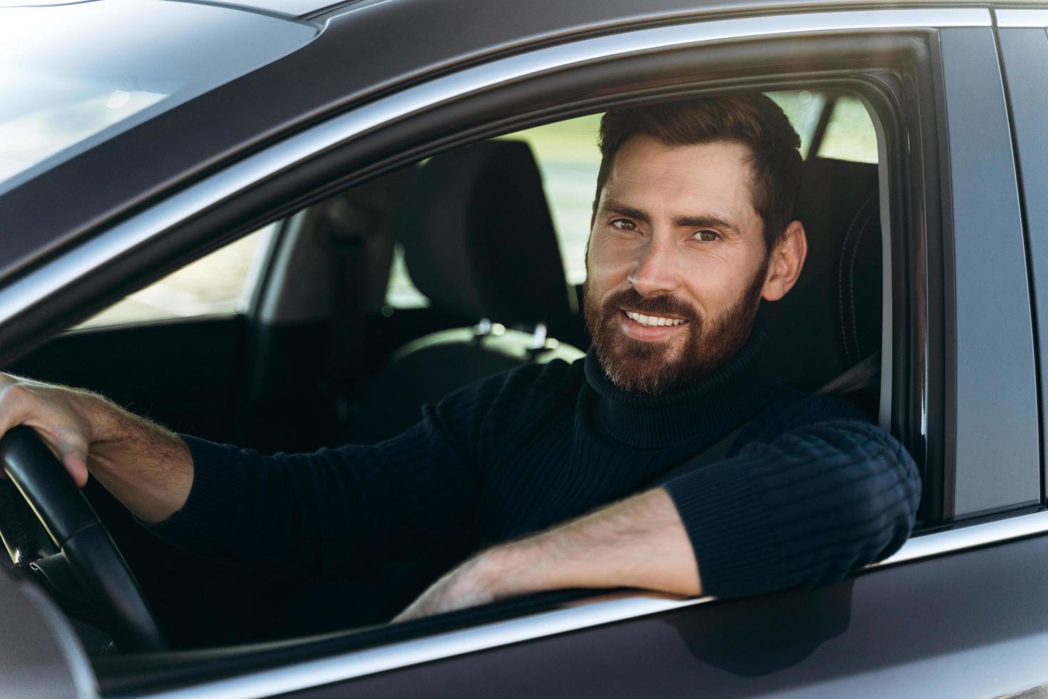 gelukkige blanke man zit en kijkt naar het raam terwijl hij een lange weg bij de auto heeft. drukke mensen en transportconcept foto