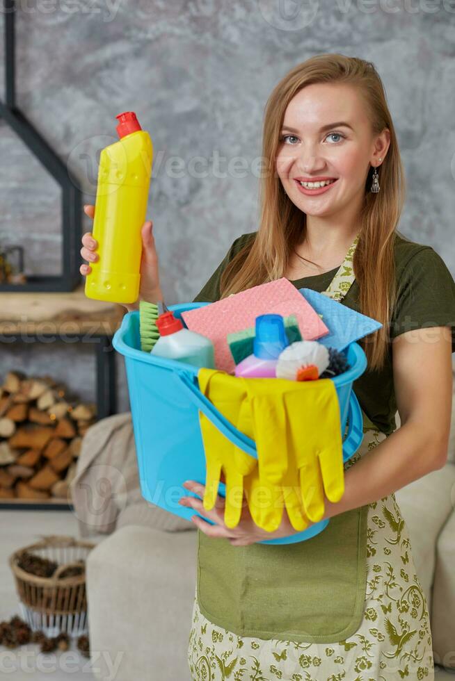 detailopname wasmiddel naar reiniging Aan emotioneel vrouw of huisvrouw handen met veel huishouden voorwerpen in blauw emmer in leven kamer. foto