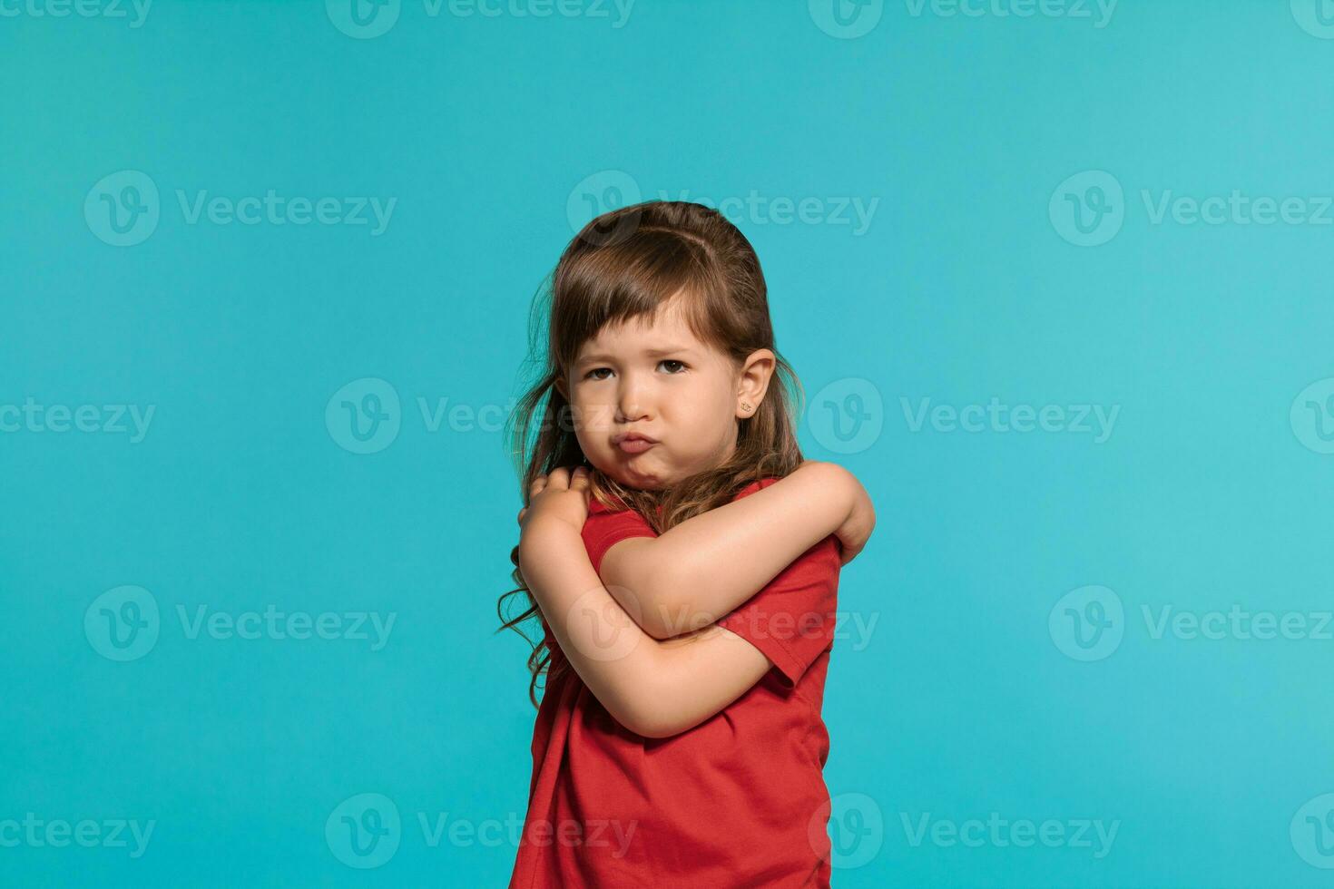 mooi weinig meisje vervelend in een rood t-shirt is poseren tegen een blauw studio achtergrond. foto