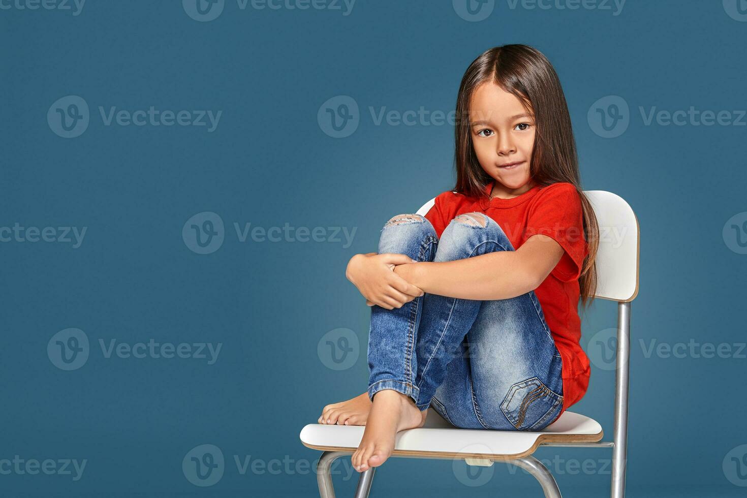 weinig meisje vervelend rood t-kort en poseren Aan stoel foto