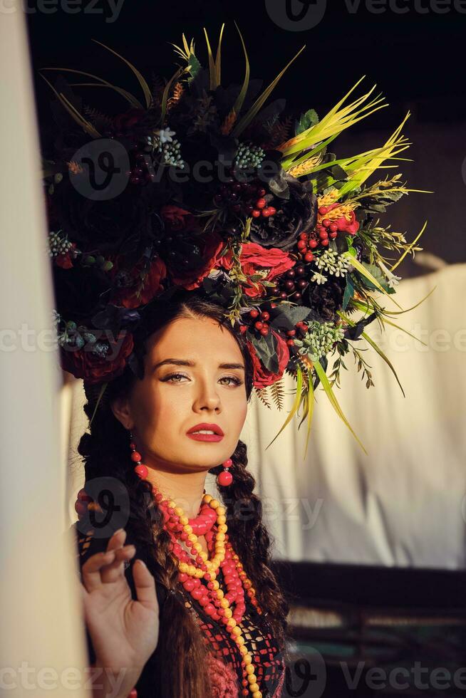 brunette meisje in een wit oekraïens authentiek nationaal kostuum en een krans van bloemen is poseren tegen een terras. detailopname. foto