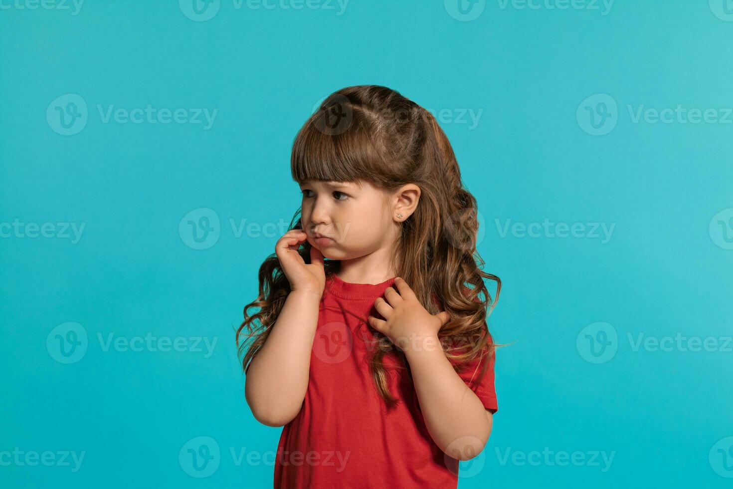 mooi weinig meisje vervelend in een rood t-shirt is poseren tegen een blauw studio achtergrond. foto