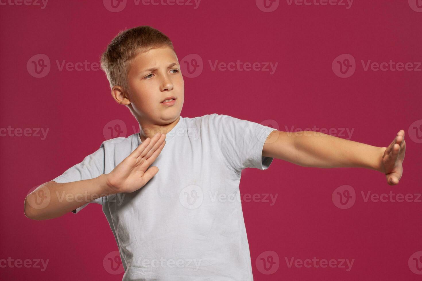 detailopname portret van een blond tiener- jongen in een wit t-shirt poseren tegen een roze studio achtergrond. concept van oprecht emoties. foto