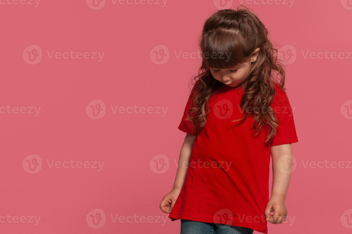 detailopname portret van een weinig brunette meisje gekleed in een rood t-shirt poseren tegen een roze studio achtergrond. oprecht emoties concept. foto