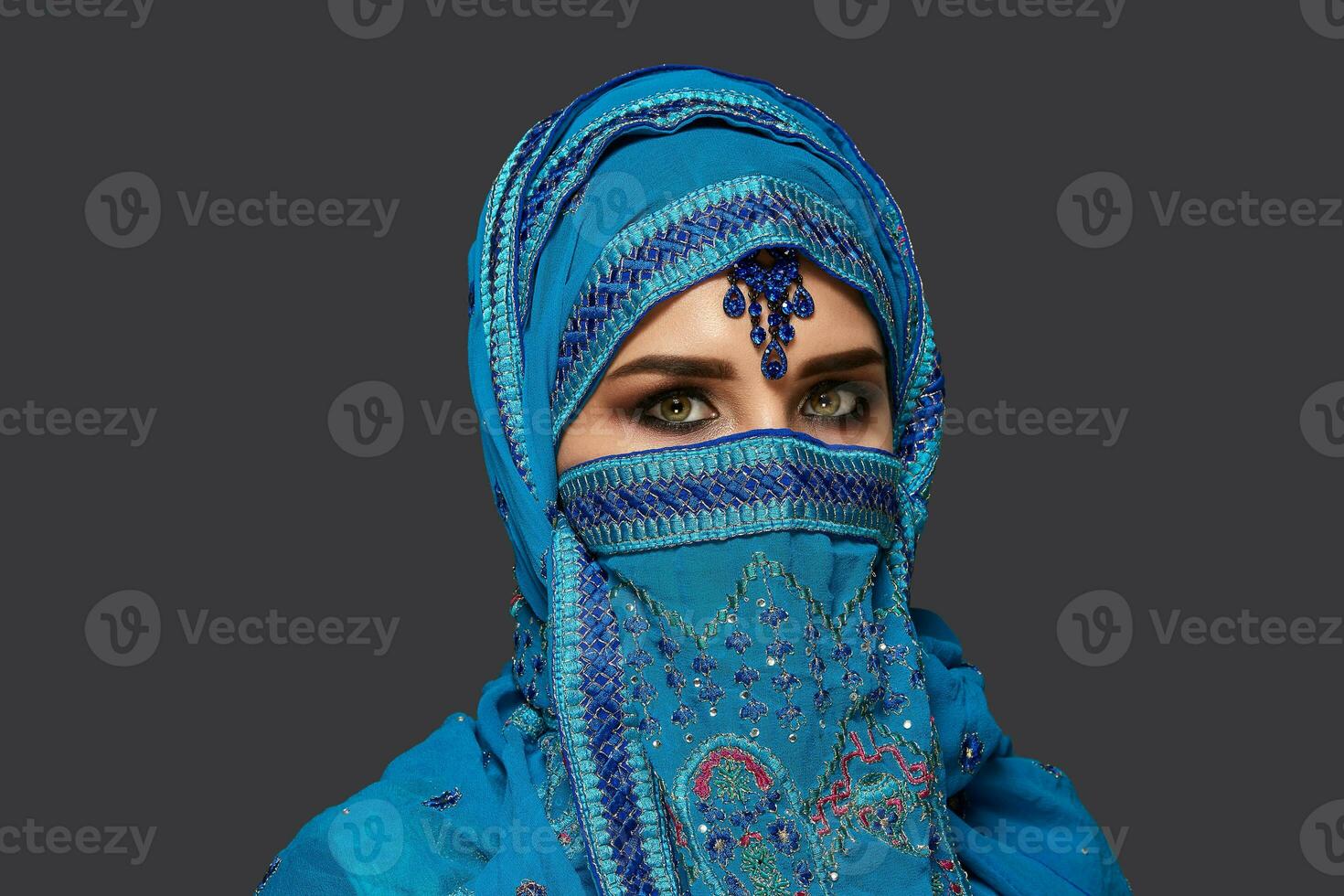 studio schot van een jong mooi vrouw vervelend de blauw hijab versierd met pailletten en sieraden. Arabisch stijl. foto