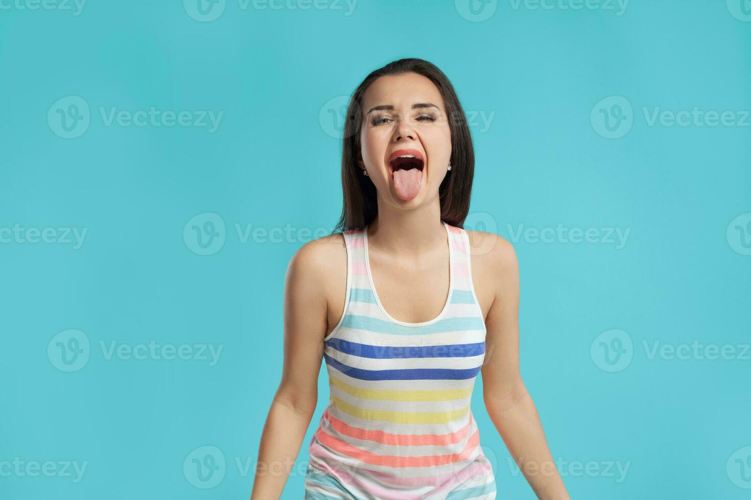 brunette vrouw met lang haar, gekleed in kleurrijk gestreept shirt, poseren tegen blauw studio achtergrond. oprecht emoties. detailopname. foto