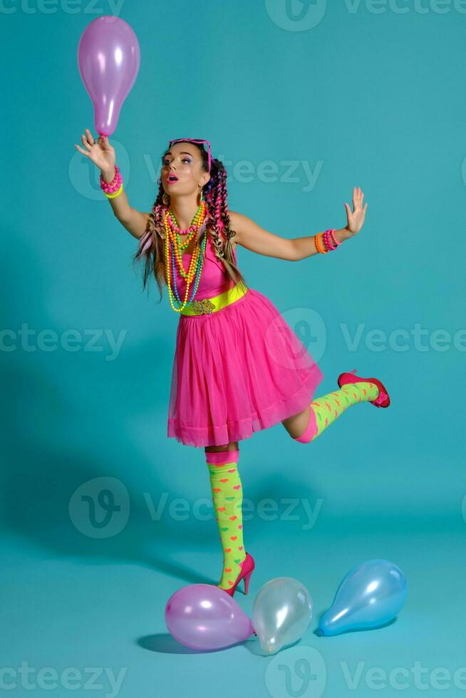 lief meisje met een veelkleurig vlechtjes kapsel en helder verzinnen, poseren in studio met lucht ballonnen tegen een blauw achtergrond. foto