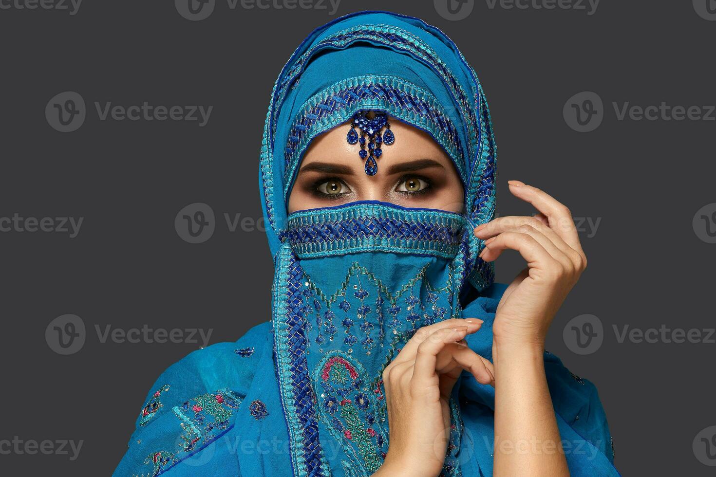 studio schot van een jong mooi vrouw vervelend de blauw hijab versierd met pailletten en sieraden. Arabisch stijl. foto