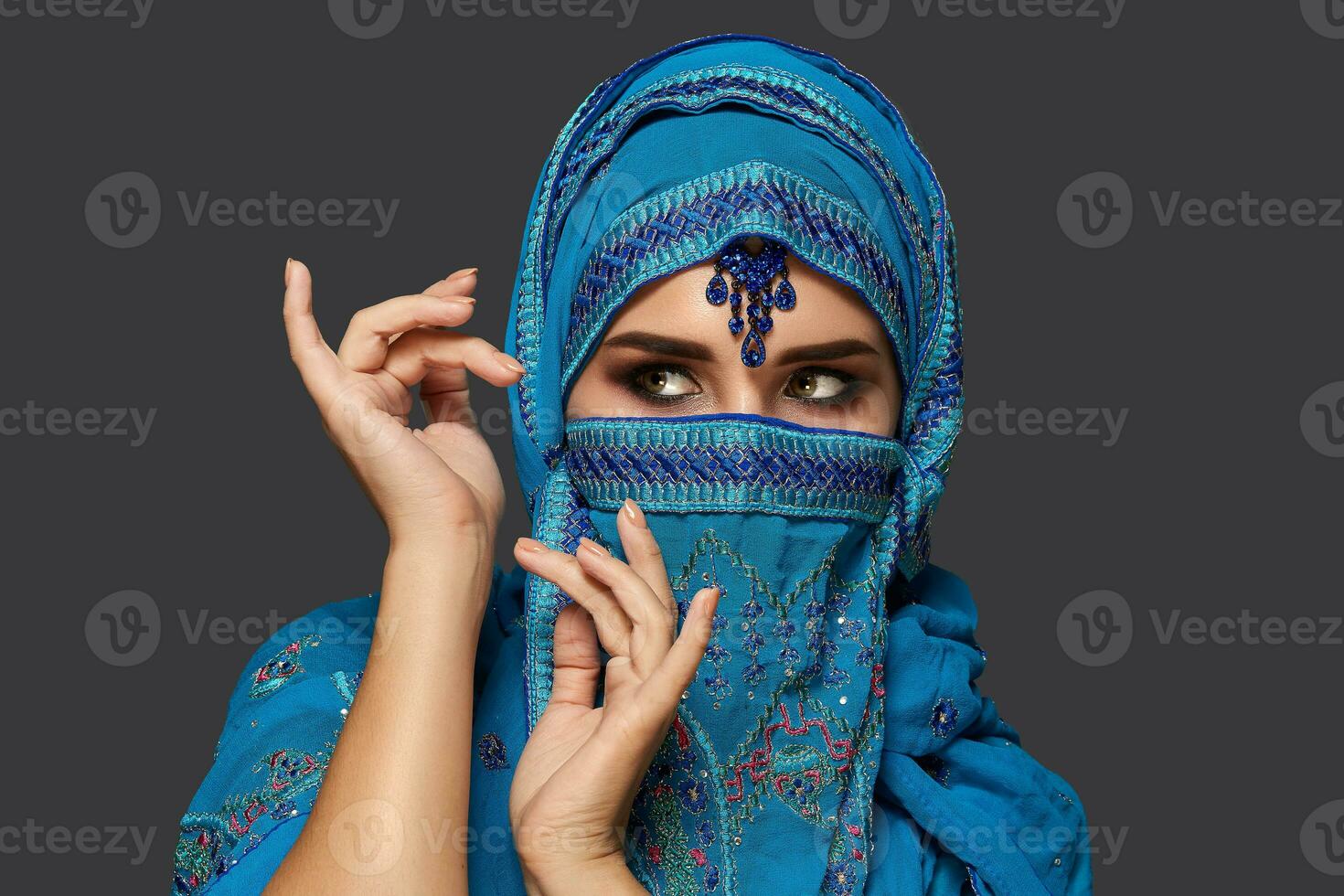 studio schot van een jong mooi vrouw vervelend de blauw hijab versierd met pailletten en sieraden. Arabisch stijl. foto