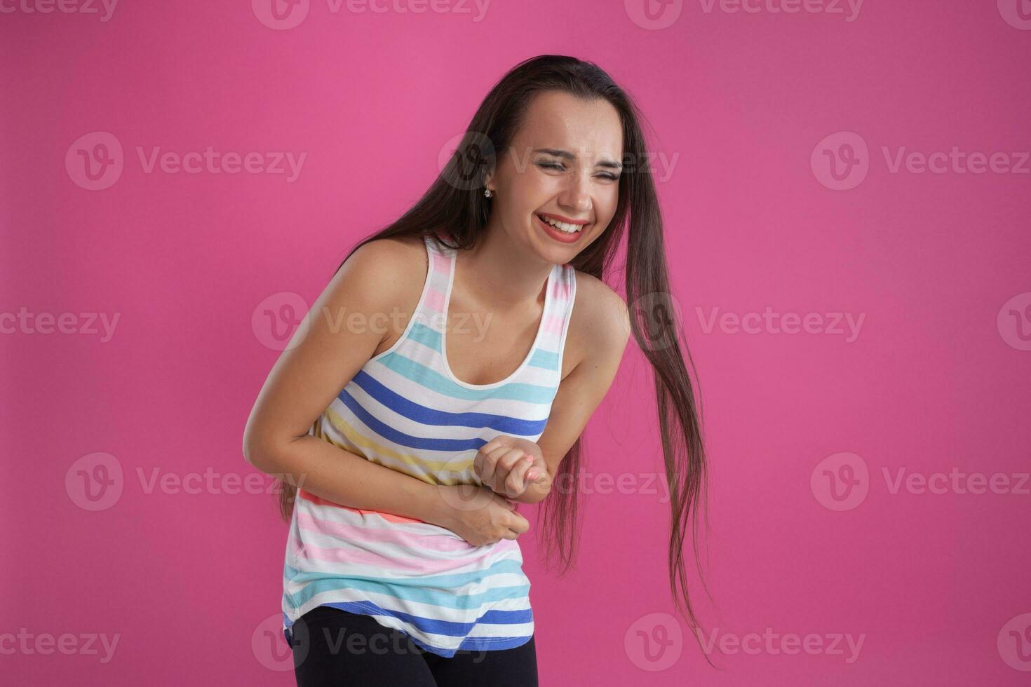 brunette vrouw met lang haar, gekleed in kleurrijk gestreept shirt, poseren tegen roze studio achtergrond. oprecht emoties. detailopname. foto