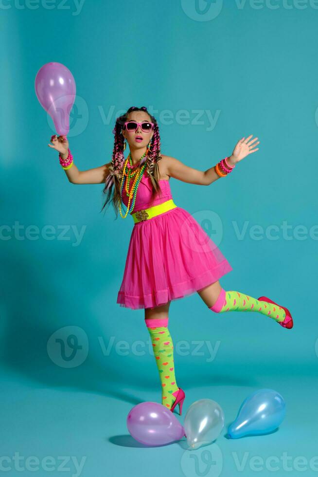 lief meisje met een veelkleurig vlechtjes kapsel en helder verzinnen, poseren in studio met lucht ballonnen tegen een blauw achtergrond. foto