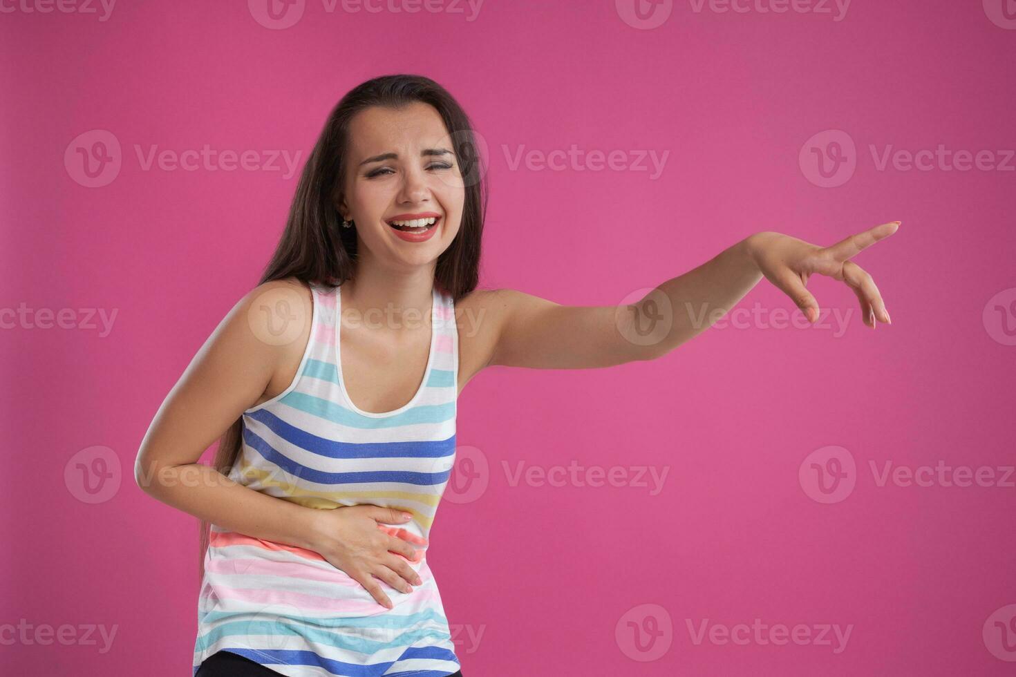 brunette vrouw met lang haar, gekleed in kleurrijk gestreept shirt, poseren tegen roze studio achtergrond. oprecht emoties. detailopname. foto