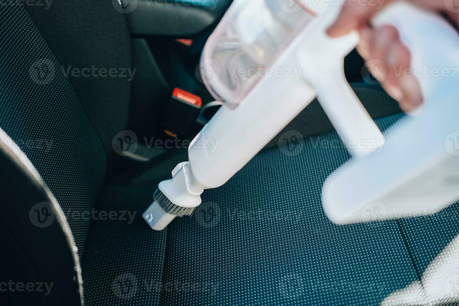 detailopname van een Mens stofzuigen een auto stoel. de hand- houdt een draadloos vacuüm schoonmaakster en reinigt de interieur van de auto. foto