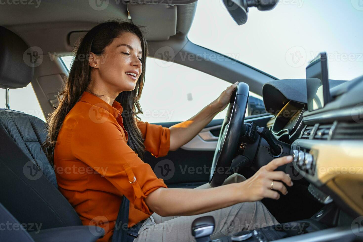 gelukkig bedrijf vrouw luisteren naar muziek- terwijl op reis met haar auto in de omgeving van de stad. vrouw draaien Aan auto lucht conditioning systeem, auto lucht conditioner Aan uit knop foto