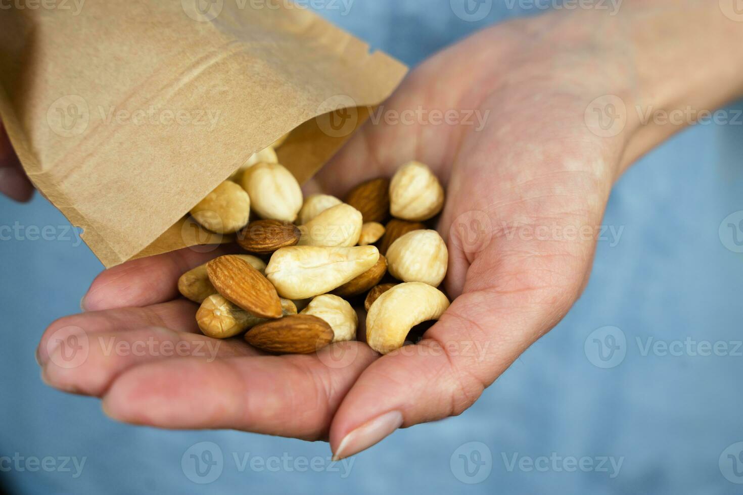 een vrouw giet een mengen van noten van een ecologisch papier zak in haar hand. gezond voedsel concept. detailopname. selectief focus. foto