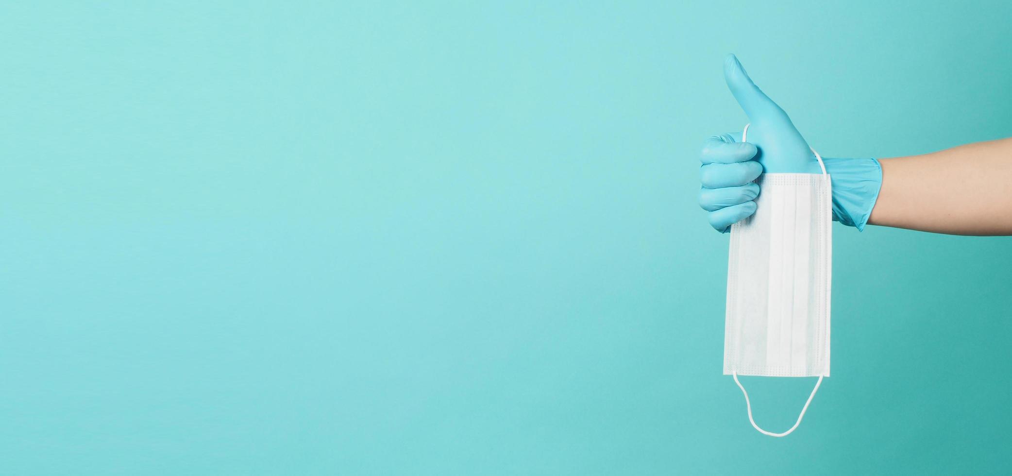 medisch masker op blauwe en groene of tiffany blauwe achtergrond. Hand dragen chirurgische handschoen en houden gezichtsmasker. en doen als handteken foto