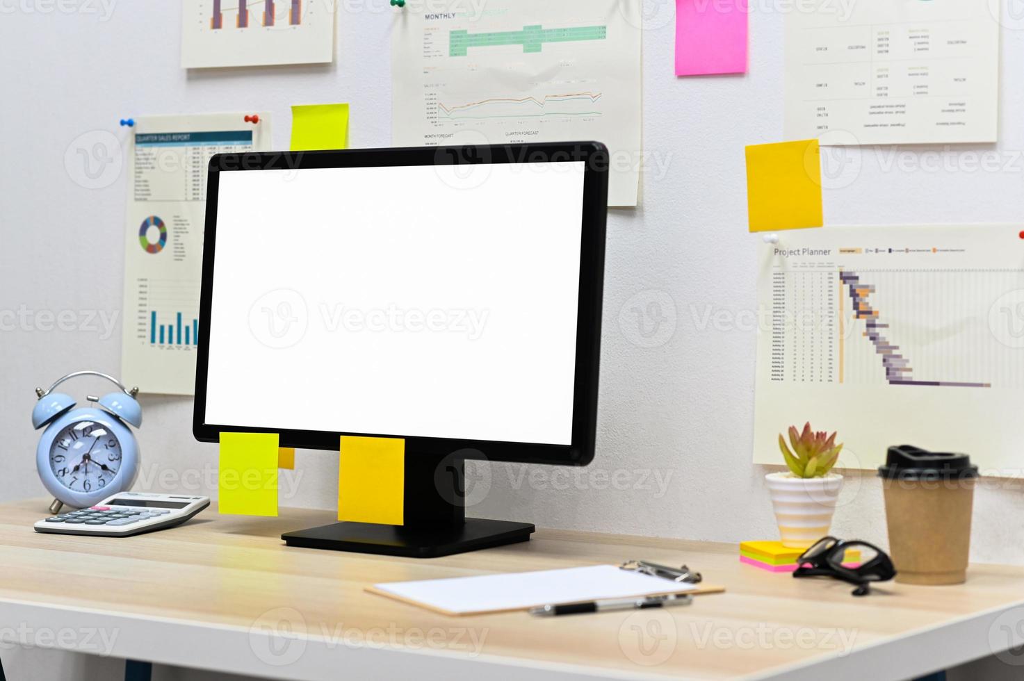 mockup leeg scherm computer met leeg klembord, klok en rekenmachine met kantoorbenodigdheden, koffie meenemen op het bureau en grafiekgegevens op kantoormuur. foto