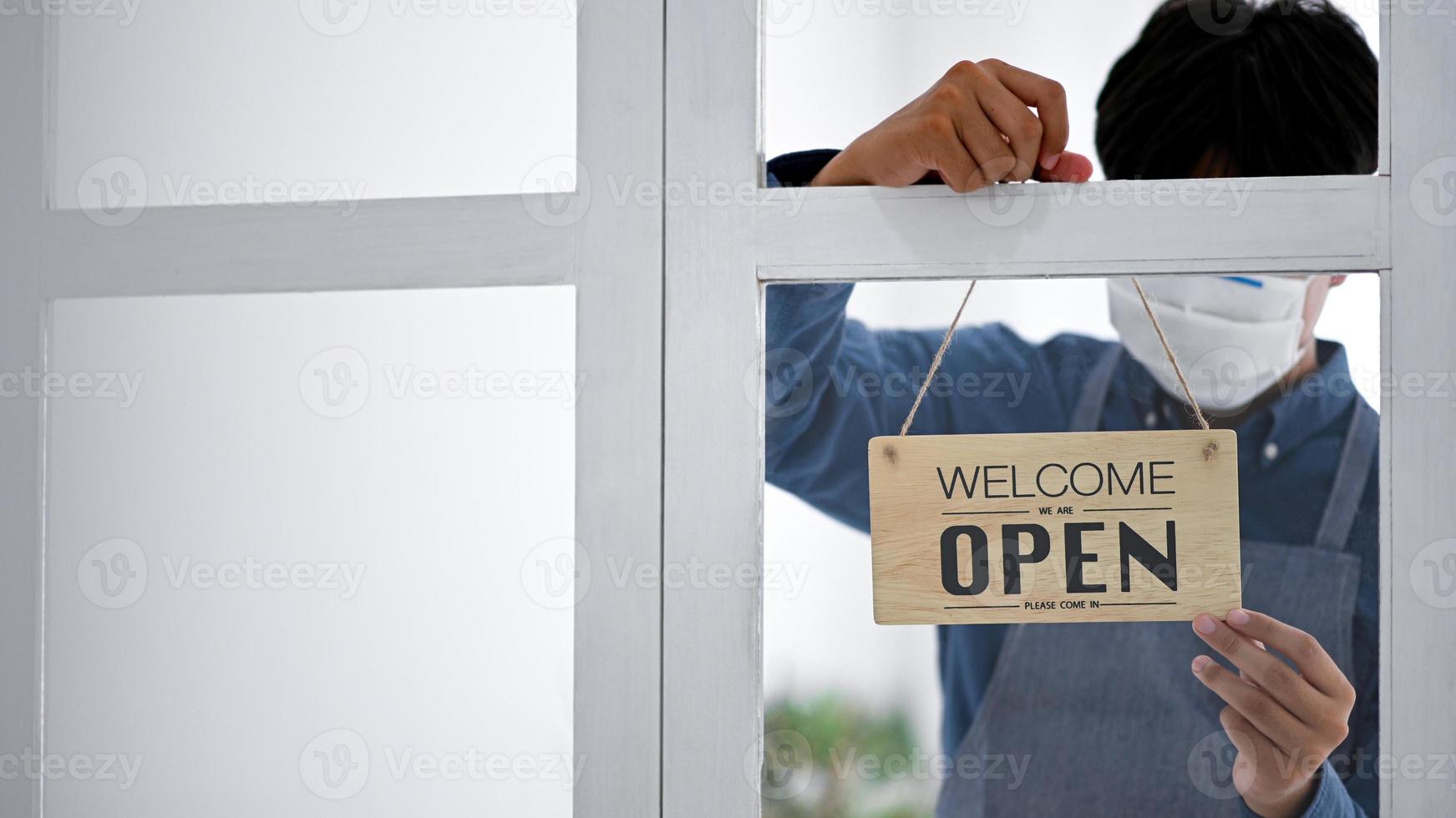 een jonge man met een masker houdt een open bord om de dienst te openen. foto