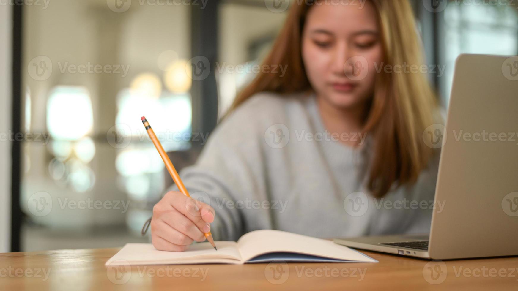 close-up shot van Aziatische tiener schrijven op notebook met laptop op bureau tijdens online les, online thuis studeren. foto