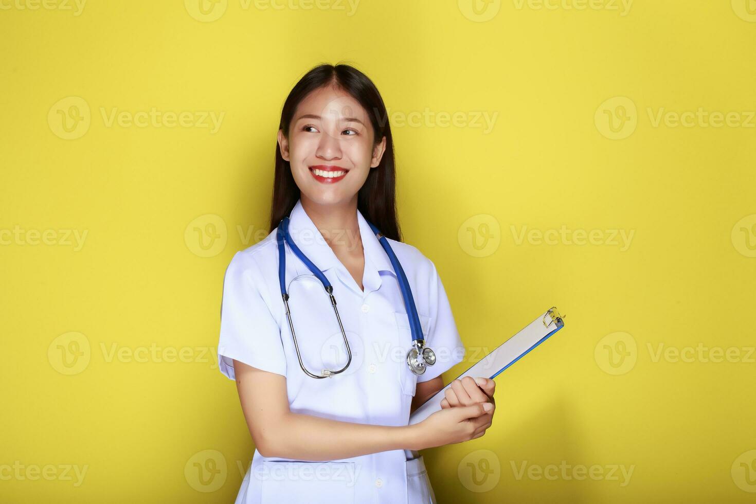 portret van een mooi jong vrouw in een geel achtergrond, Aziatisch vrouw vervelend een dokter uniform maakt een glimlachen uitdrukking, een jong vrouw vervelend een medisch stethoscoop heeft een vriendelijk uitdrukking. foto