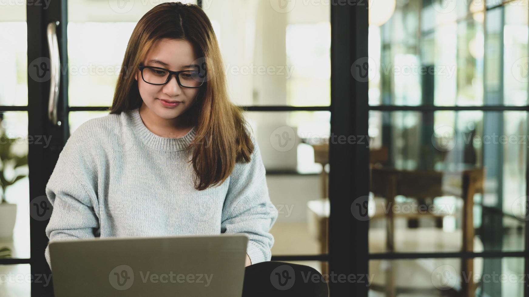 aziatische vrouw met een bril die neerkijkt op laptop, ze werkt in een coffeeshop, vooraanzicht geschoten. foto