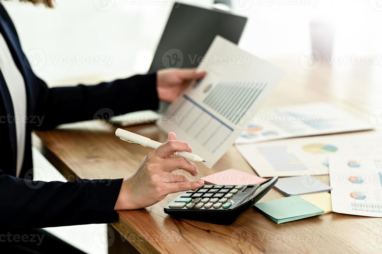 een zakenvrouw in een pak gebruikt een rekenmachine en houdt een grafiek vast. foto