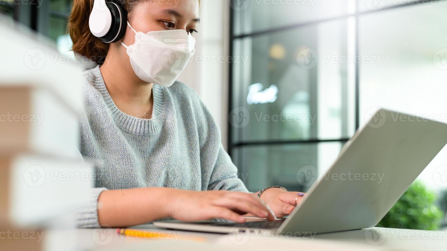 een jonge vrouw met een koptelefoon en een masker gebruikt een laptop. foto