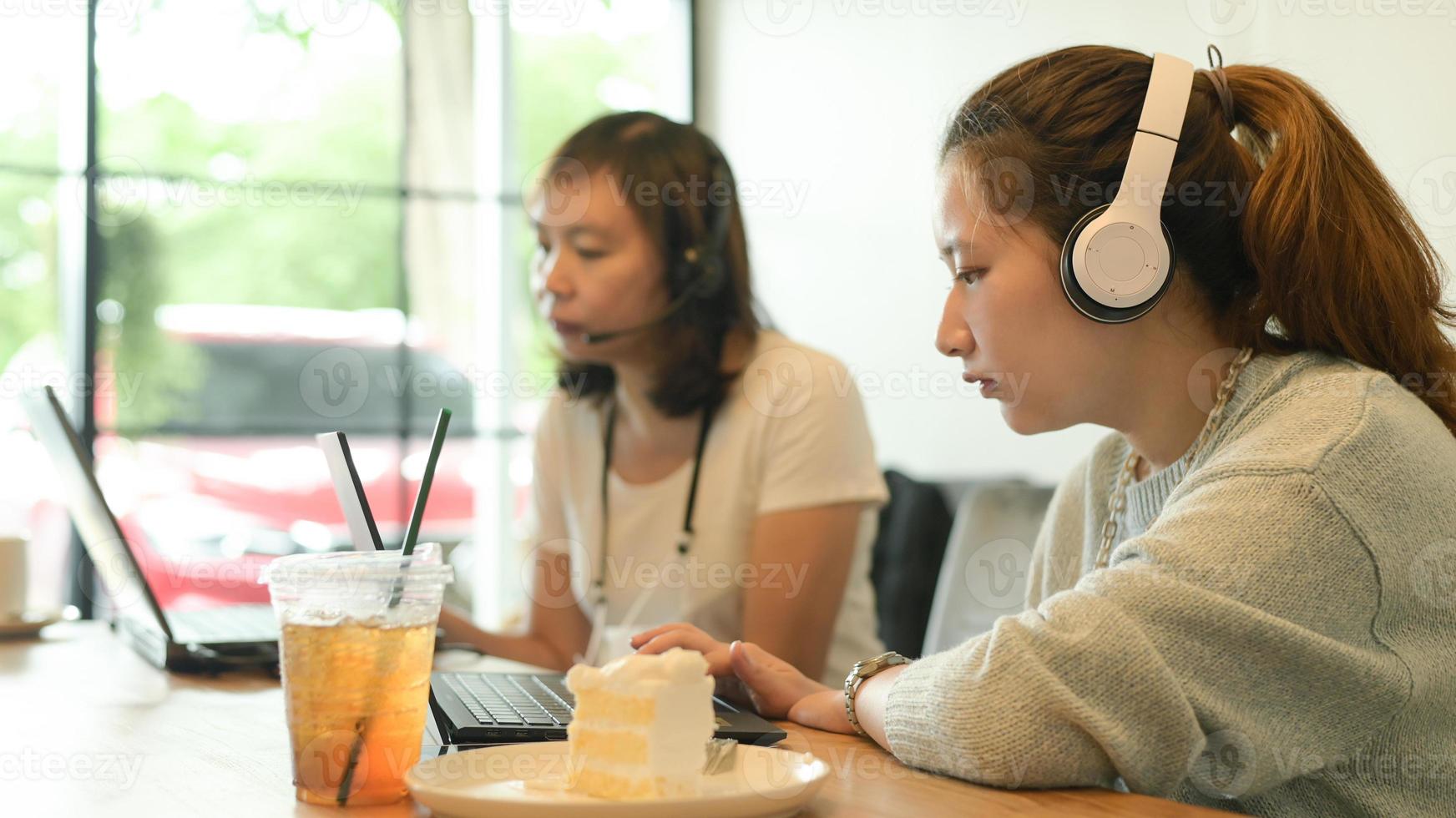 twee jonge vrouwen die hoofdtelefoons dragen die met laptops in een koffiewinkel werken. foto