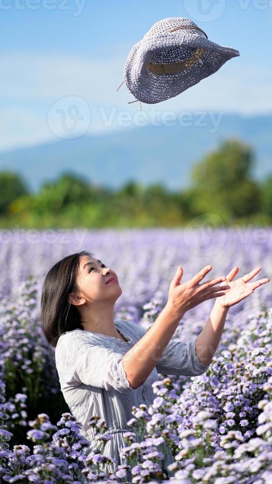 aziatische vrouw die gelukkig in een bloementuin poseert en een hoed gooit terwijl ze een foto maakt.