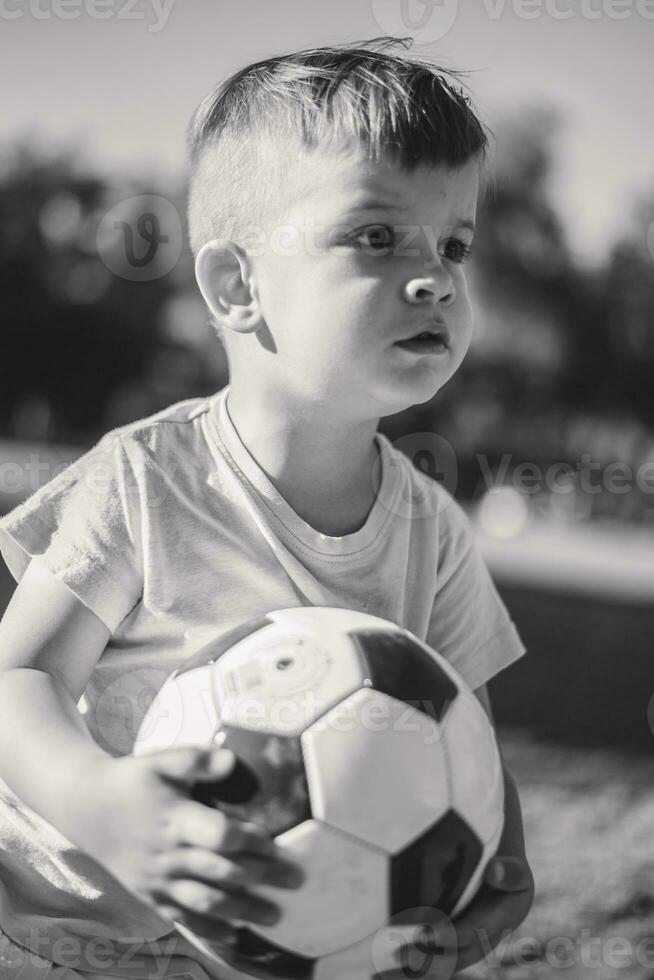 weinig jongen spelen met een voetbal bal Aan de veld- in zomer foto