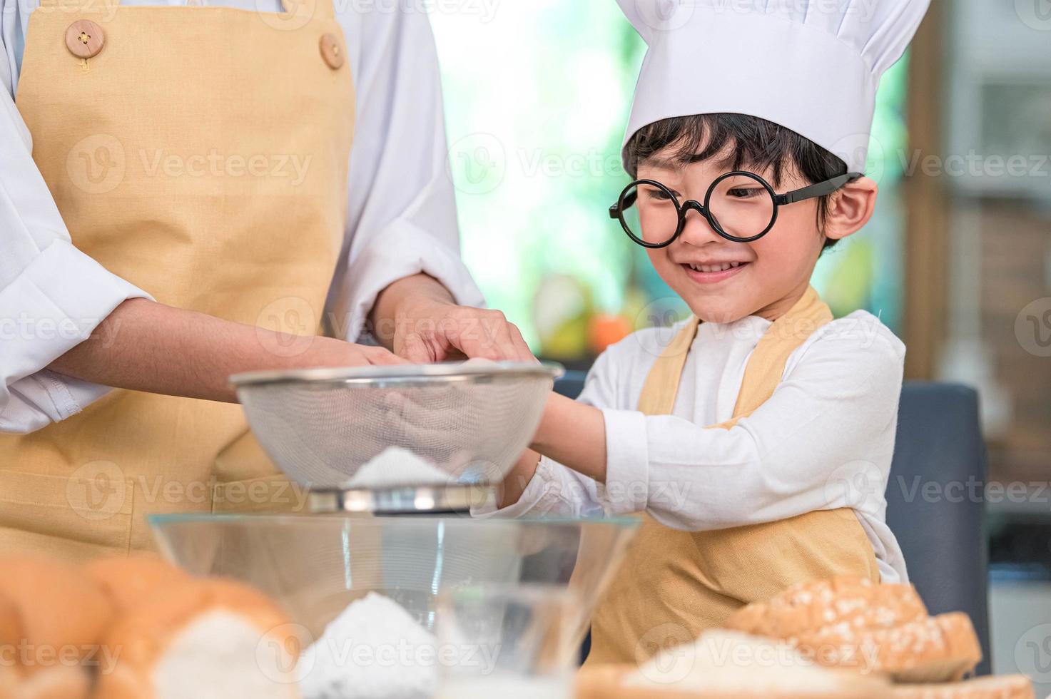 schattige kleine aziatische jongen en mooie moeder die deegmeel zeven met zeefzeefvergiet in huiskeuken op tafel om zich voor te bereiden op het bakken van bakkerij en cake. Thaise kinderen spelen met meel als chef grappig foto