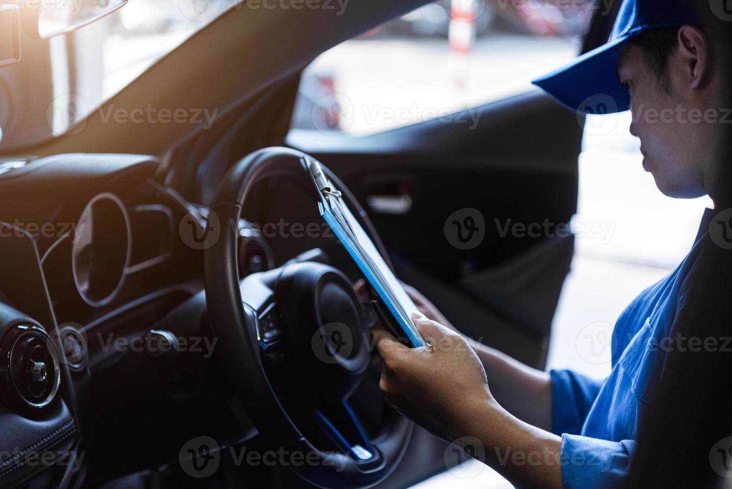 monteur die klembord vasthoudt en in de auto naar het onderhoudsvoertuig controleert door de bestelling van de klant in de garage van de autoreparatiewerkplaats. reparatie service. mensen beroep en zakelijke baan. auto technicus foto