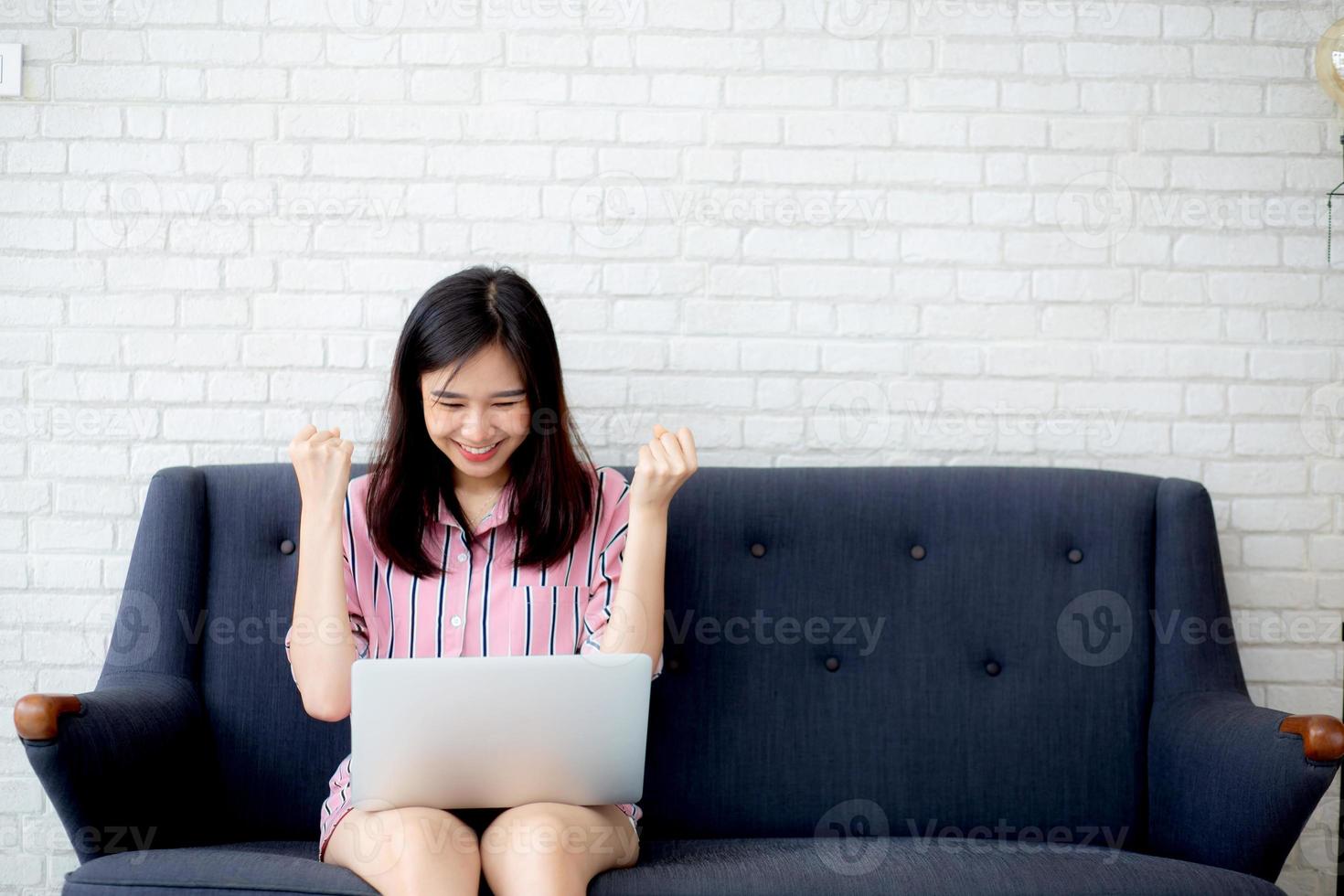 jonge aziatische vrouw opgewonden en blij met succes met laptop op de bank. foto