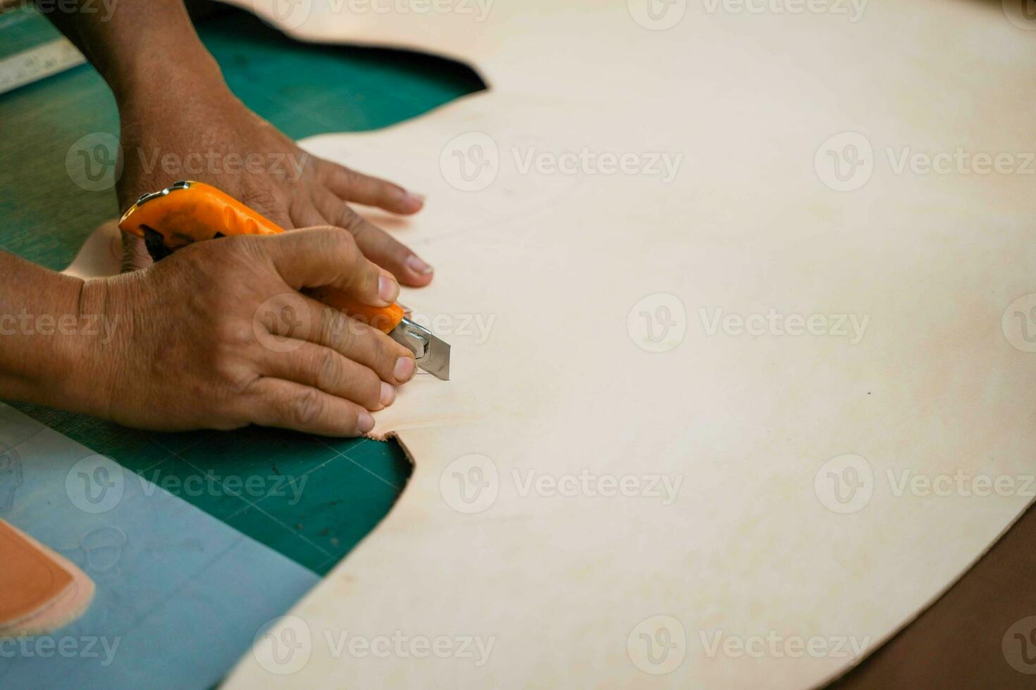 detailopname en Bijsnijden handen van leer vakman is gebruik makend van een snijder mes naar besnoeiing een stuk van wit leer groot vel volgens naar de ontwerp naar brengen uit naar naaien in producten voor klanten. foto