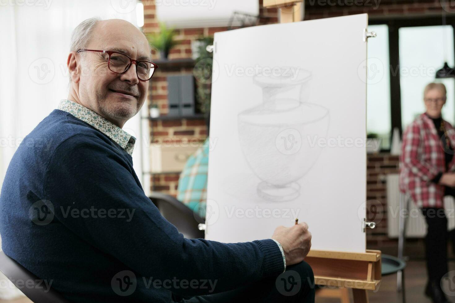 gelukkig volwassen Mens glimlachen Bij camera terwijl tekening met potlood Aan canvas, senior mensen aan het leren nieuw vaardigheid, genieten van creatief activiteiten in pensioen, nemen omhoog kunst werkzaamheid Bij lokaal gemeenschap centrum foto