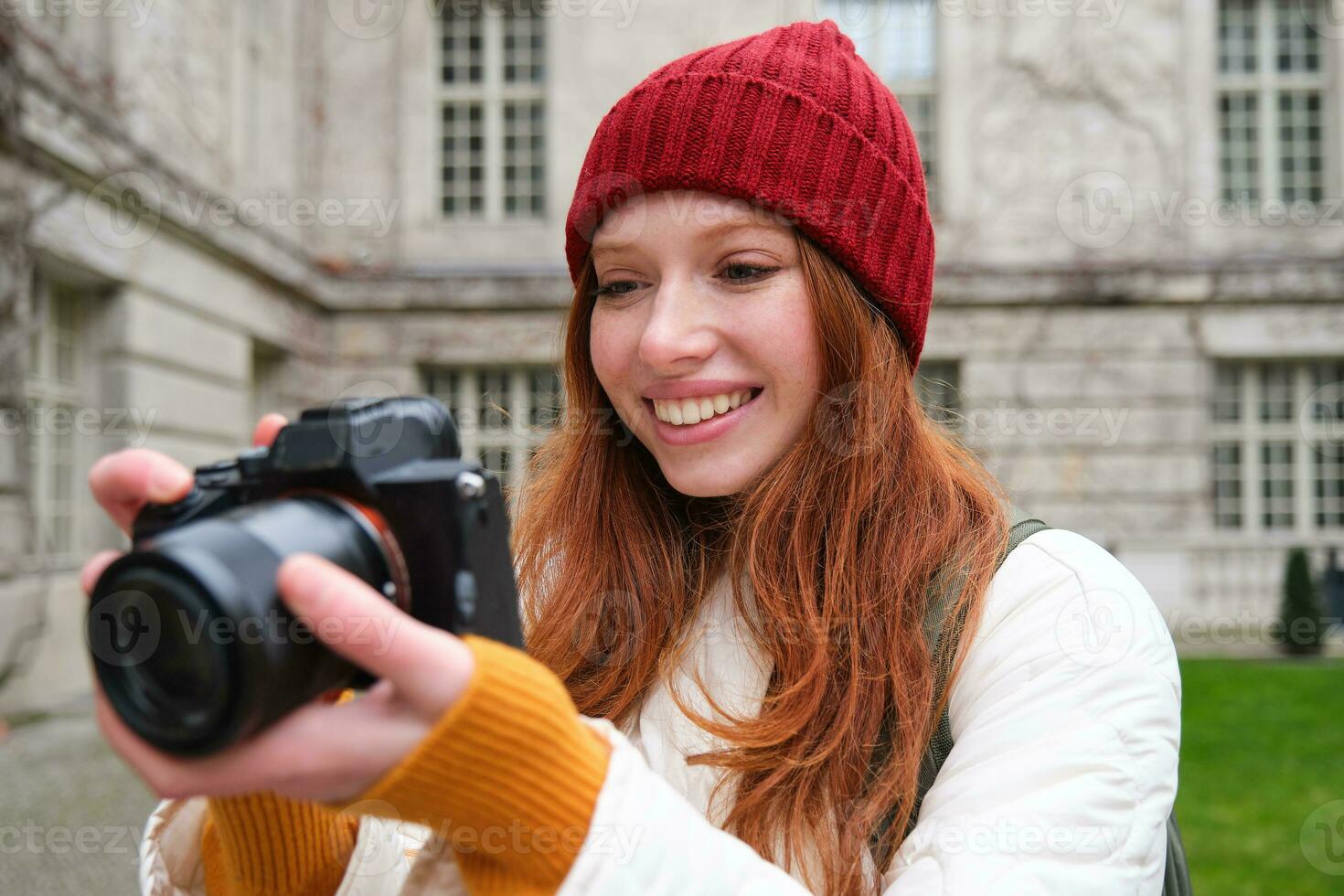 roodharige meisje fotograaf duurt foto's Aan professioneel camera buitenshuis, vangt Street Style schoten, looks opgewonden terwijl nemen afbeeldingen foto