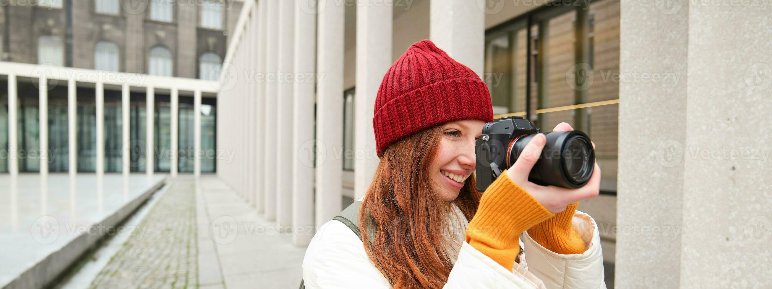glimlachen roodharige meisje fotograaf, nemen afbeeldingen in stad, maakt foto's buitenshuis Aan professioneel camera foto