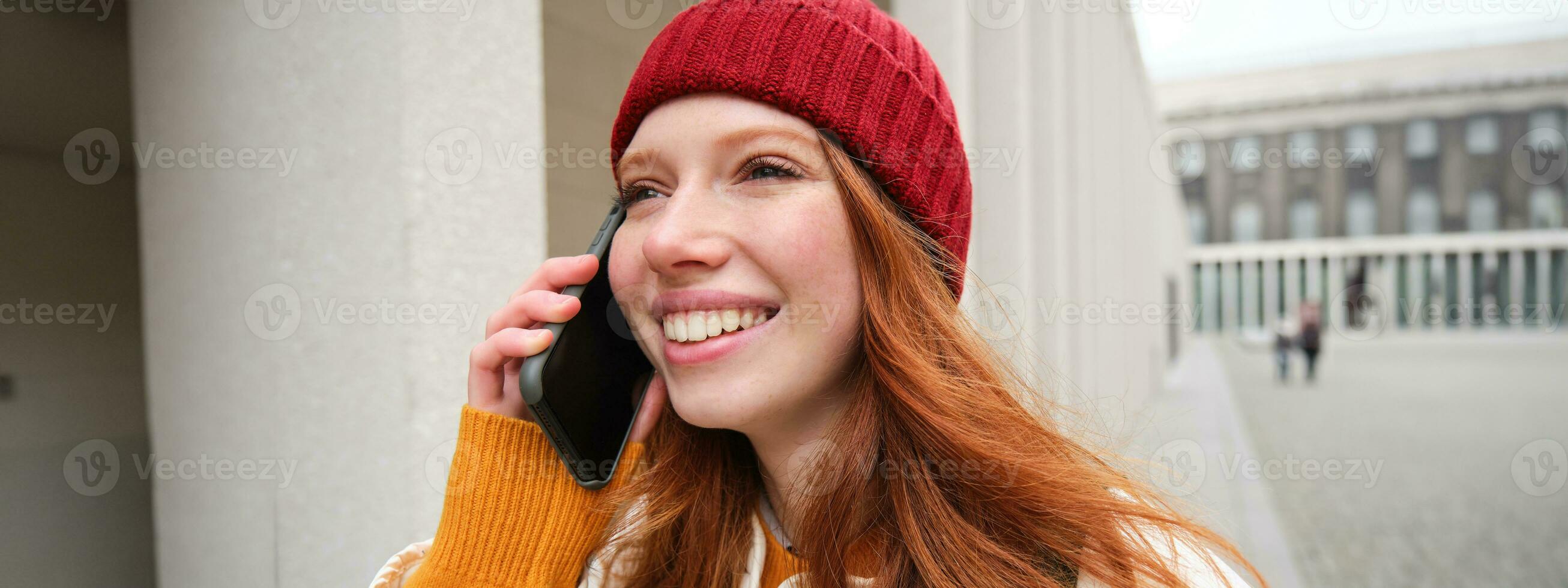 gelukkig roodharige vrouw, meisje met telefoon gesprekken, heeft gesprek Aan mobiel app, toepassingen internet naar telefoontje Buitenland met smartphone app, lachend en glimlachen foto