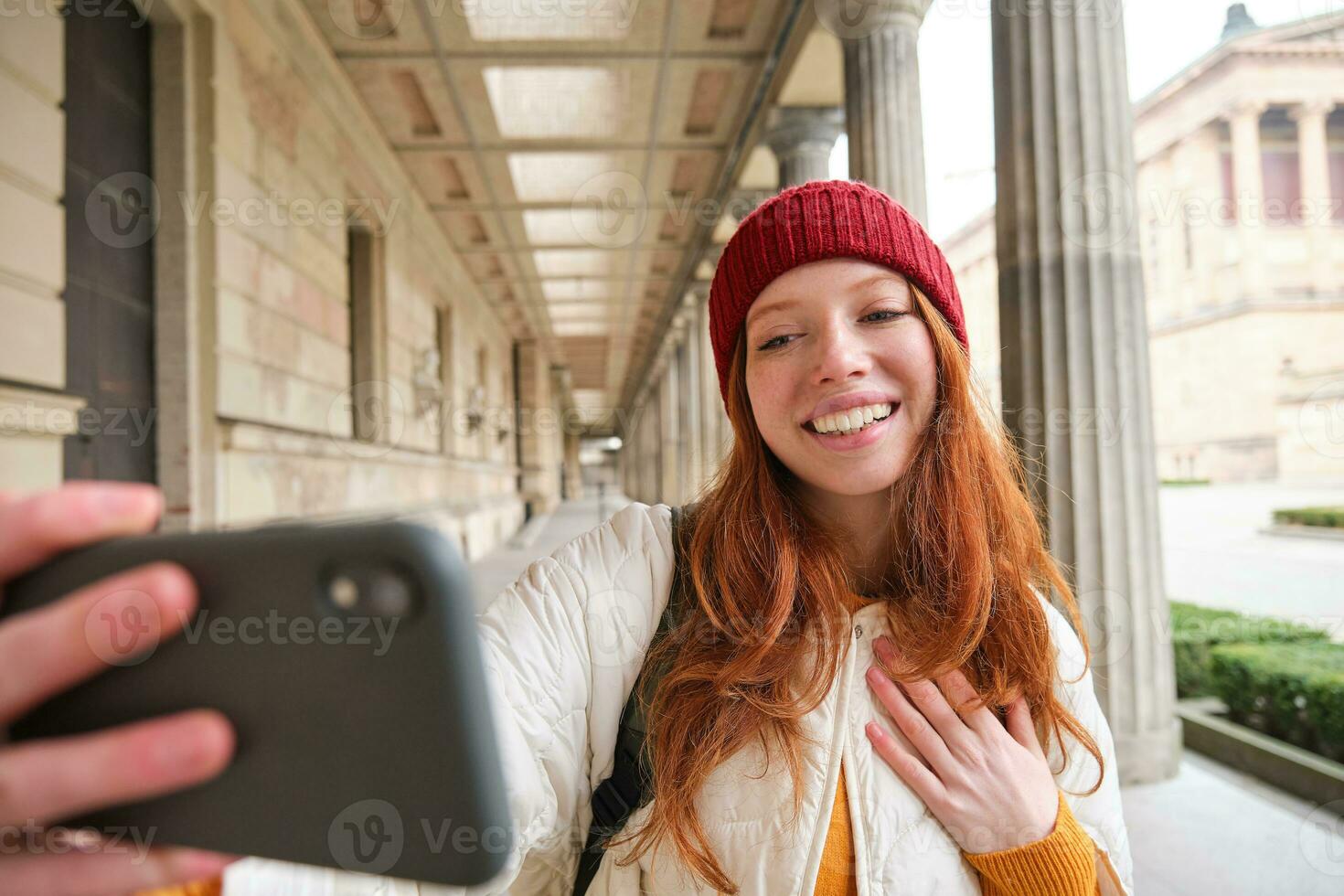 schattig jong roodharige vrouw duurt selfie Aan straat met mobiel telefoon, maakt een foto van haarzelf met smartphone app Aan straat