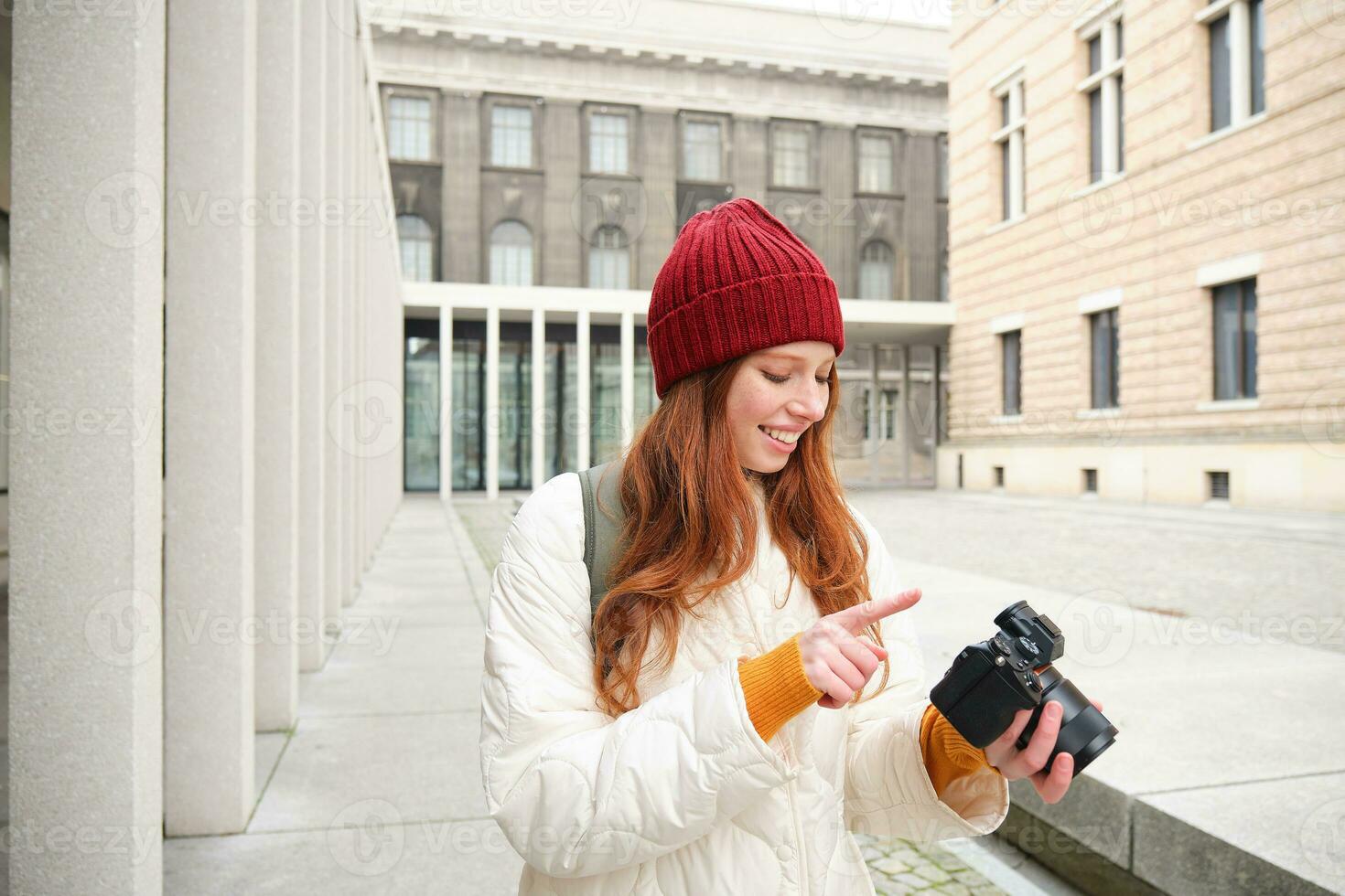 glimlachen roodharige meisje fotograaf, nemen afbeeldingen in stad, maakt foto's buitenshuis Aan professioneel camera foto