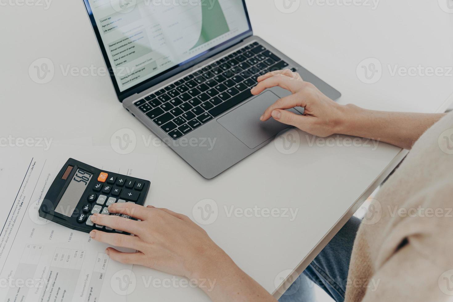onherkenbare vrouw zit aan bureau met laptop computer rekenmachinepapieren berekent maandelijkse uitgaven foto
