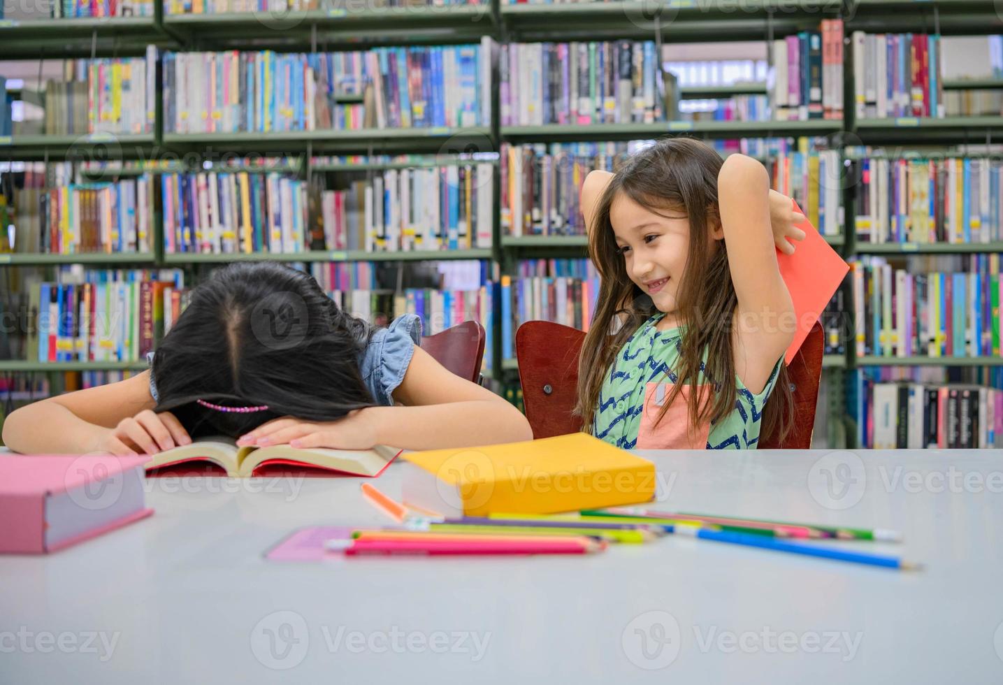 geluk twee schattige diversiteitsmeisjes die een boek lezen en plagen om slapende vriend in de schoolbibliotheek grappig te raken. mensen levensstijl en onderwijs en vriendschap. kind en kinderen groepsactiviteit vrije tijd foto